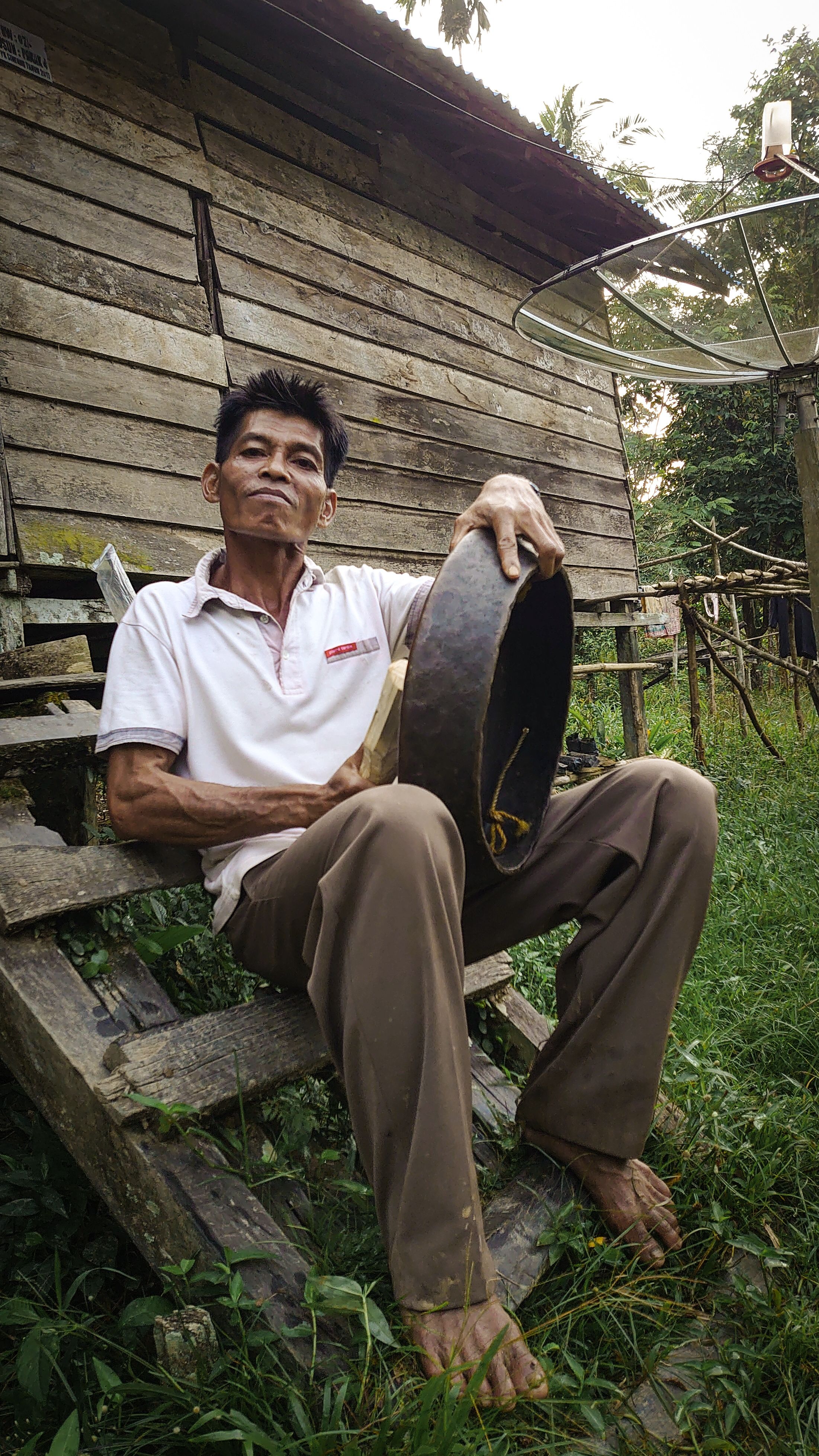 Indonesian man relaxing on stairs by a rustic wooden house in West Kalimantan.