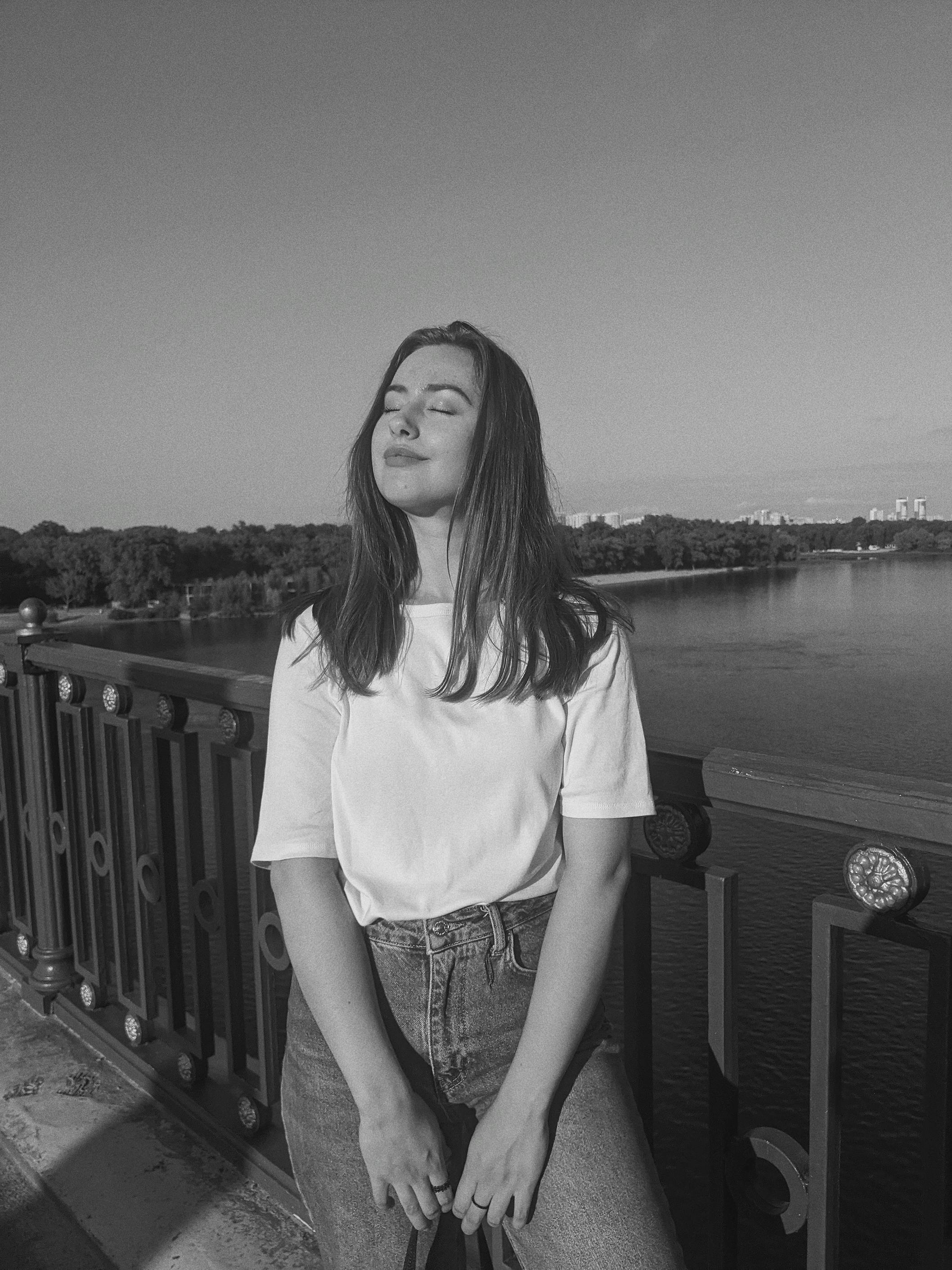 A woman enjoys a tranquil moment on a riverside bridge in monochrome.