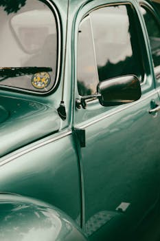 A detailed view of a classic green car, showcasing its retro design and side mirror.