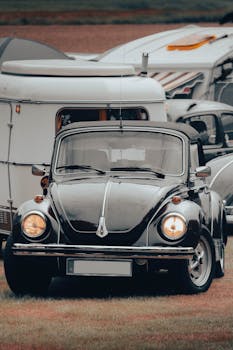 Vintage Volkswagen Beetle parked outdoors by a caravan on grass.