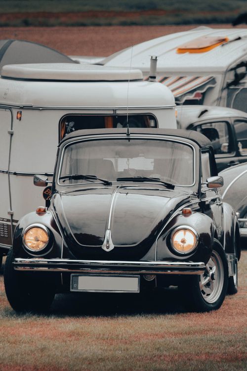Free Vintage Volkswagen Beetle parked outdoors by a caravan on grass. Stock Photo
