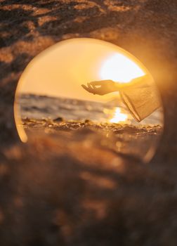 Artistic photo of a hand silhouetted against a sunset in a beach reflection, capturing tranquility.