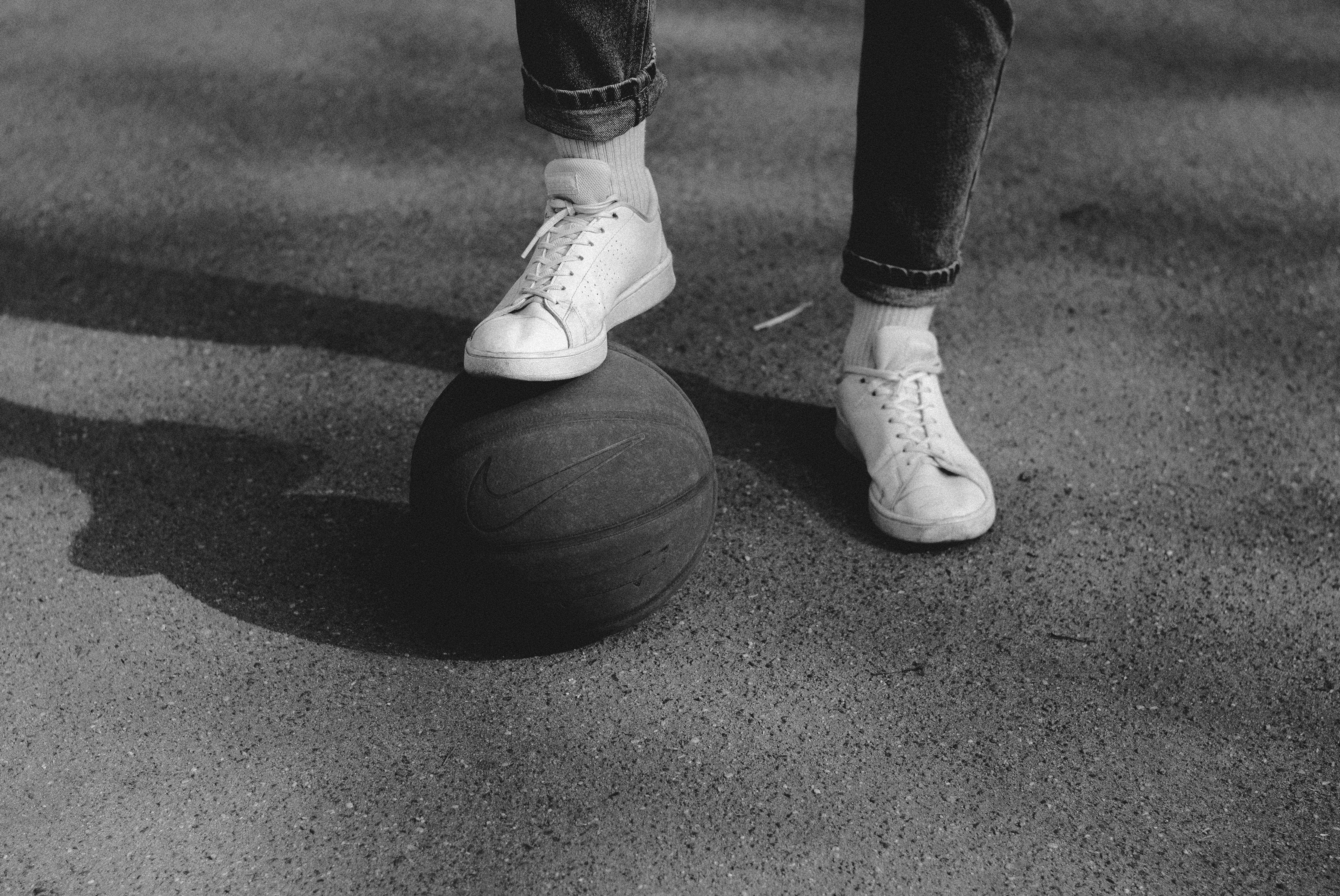 person in black pants and white nike sneakers standing on basketball ball in grayscale photography