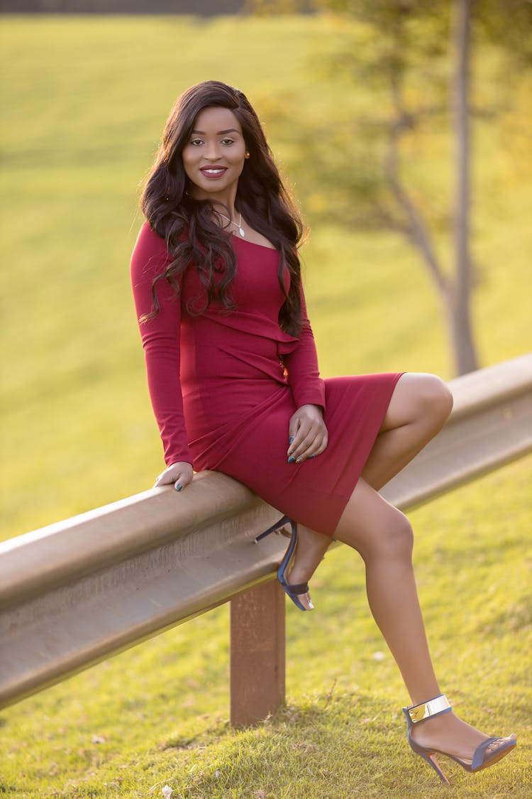 Woman In Red Dress Wearing Blue Heels Sitting On Barrier 