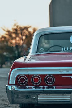 A rear view of a classic red vintage car parked outdoors during sunset, capturing retro charm.
