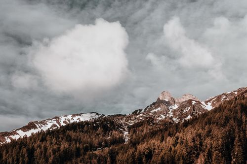 Free A breathtaking view of snow-capped mountains and lush forests under a dramatic cloudy sky. Stock Photo