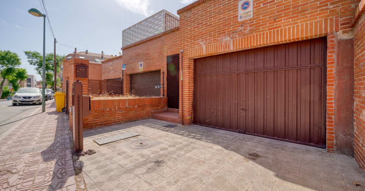 Sunny day outside a red brick house with garage in a quiet neighborhood.
