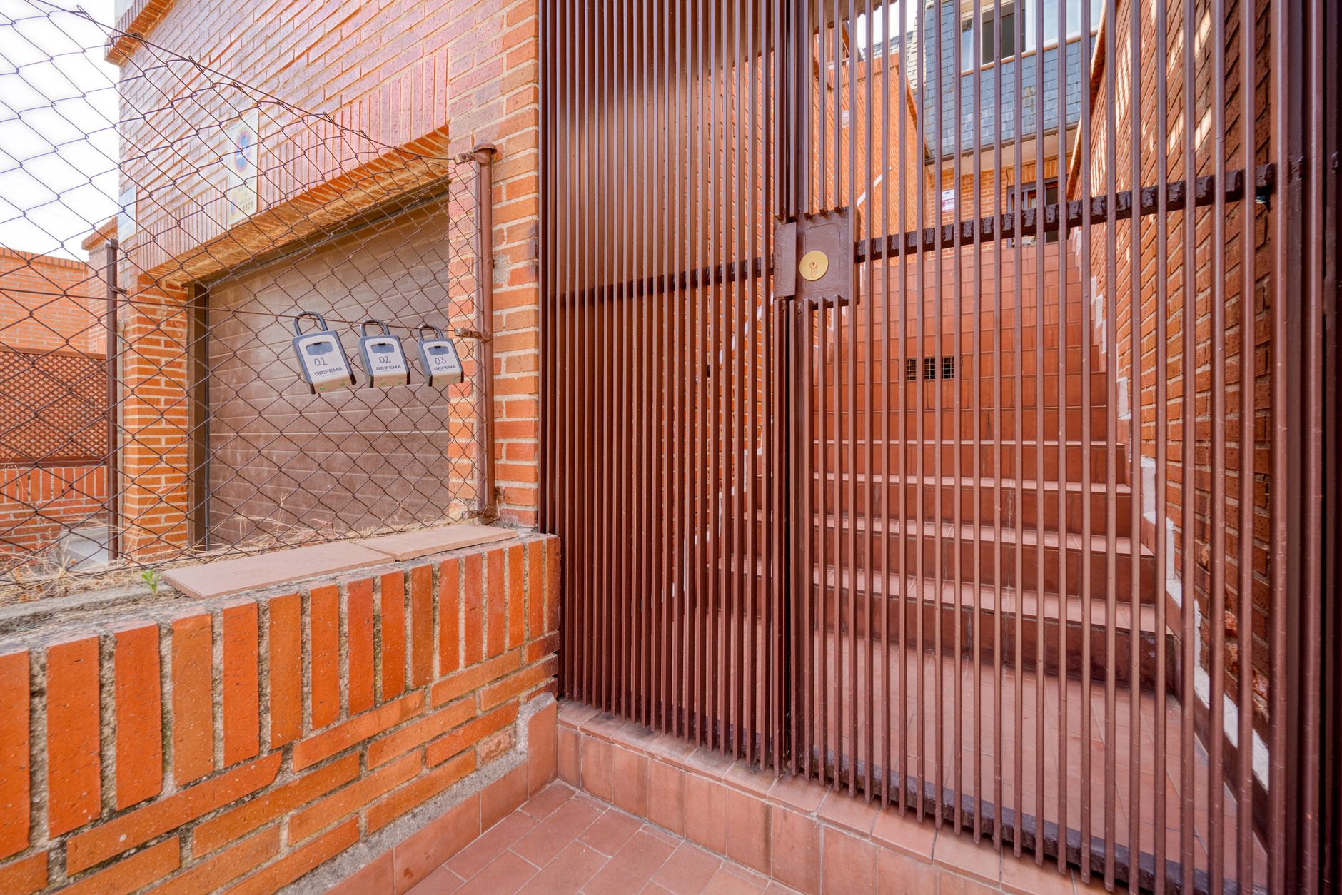 Secure brick residential entrance with brown metal gates and steps in view.