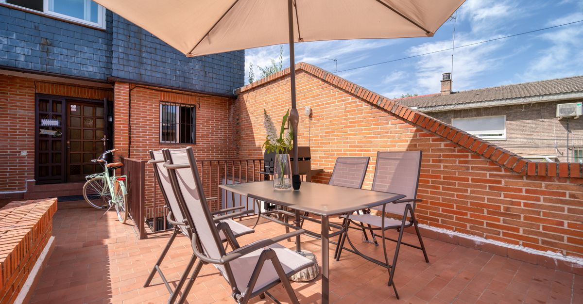 A cozy outdoor terrace with chairs, table, and umbrella under the blue sky.