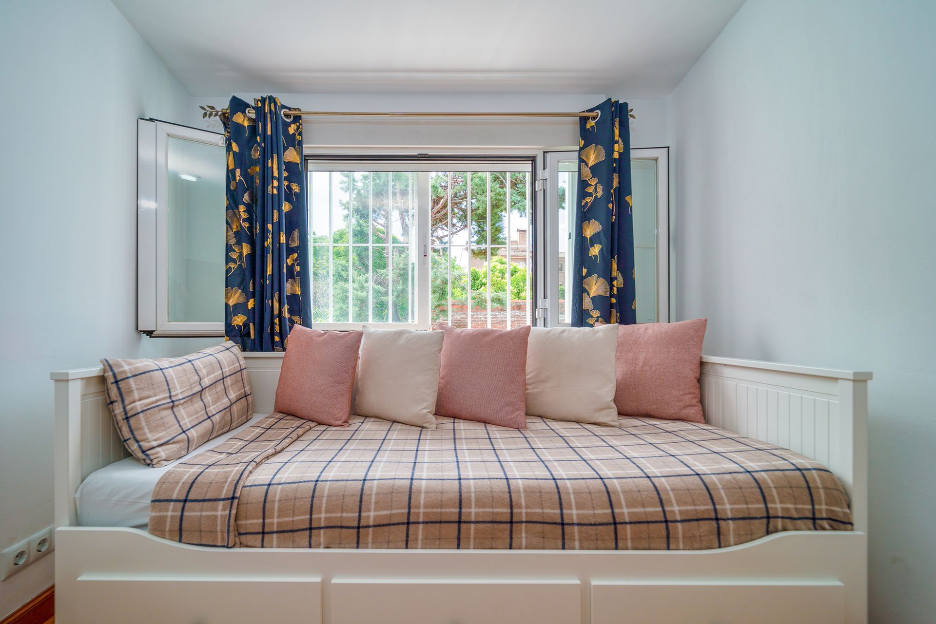 Minimalist bedroom with a cozy daybed and plaid bedding near a window.