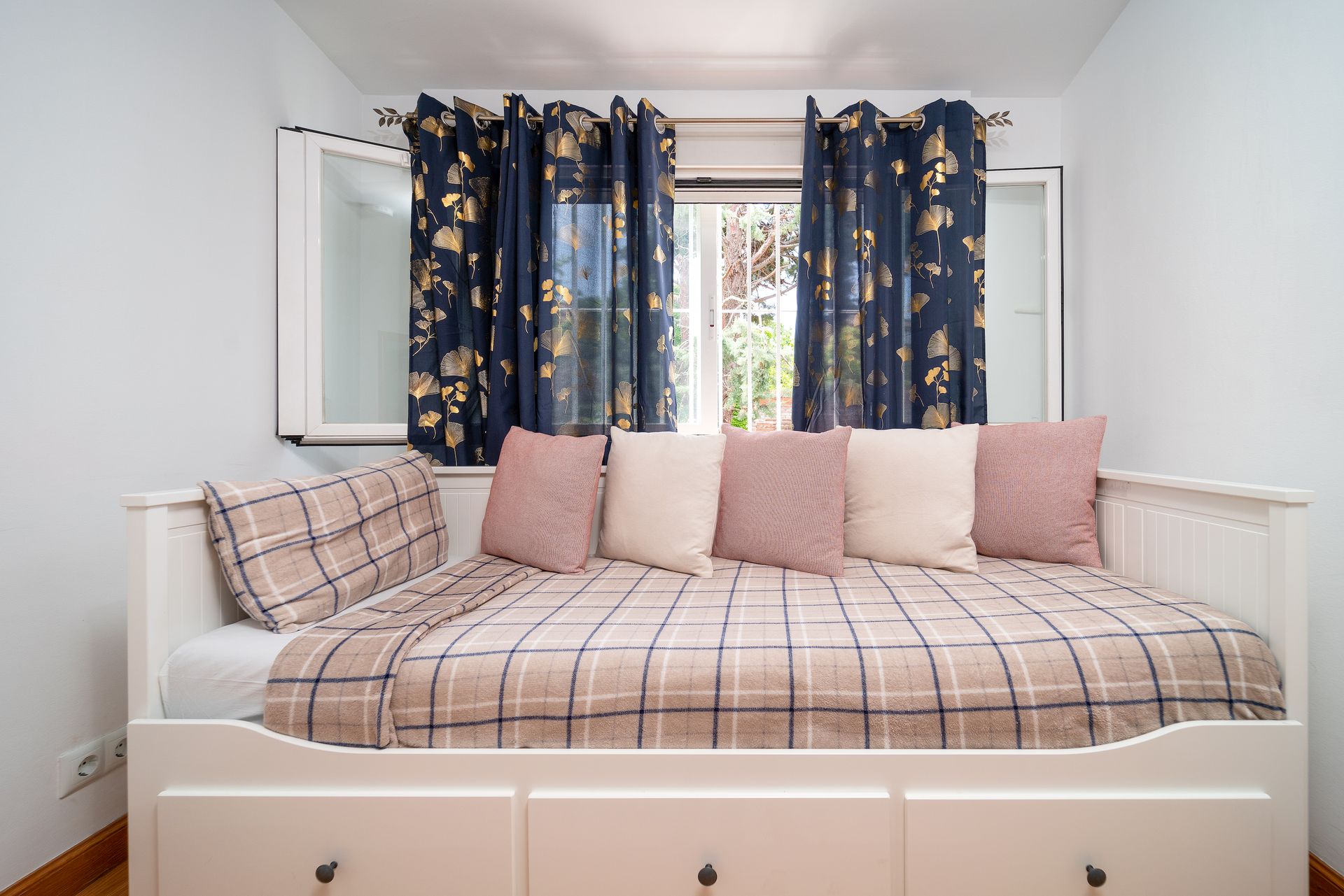 Charming minimalist bedroom featuring a comfortable daybed with plaid bedding and floral curtains.