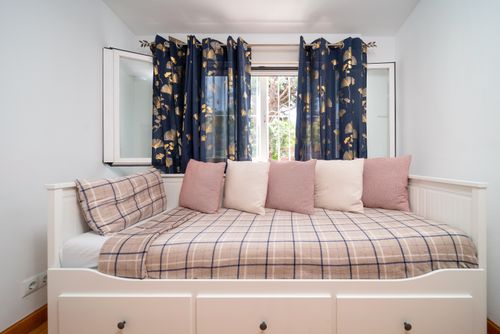 Free Charming minimalist bedroom featuring a comfortable daybed with plaid bedding and floral curtains. Stock Photo