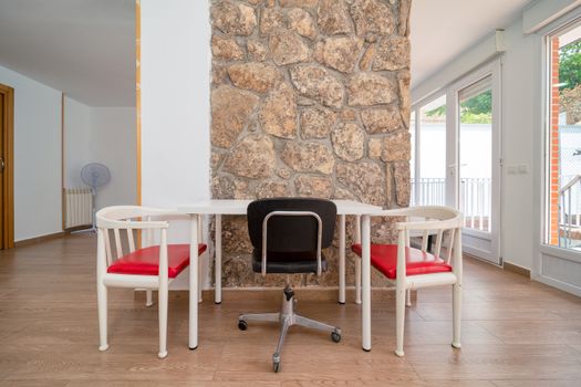 Bright modern dining area featuring red and white chairs with a stone accent wall.