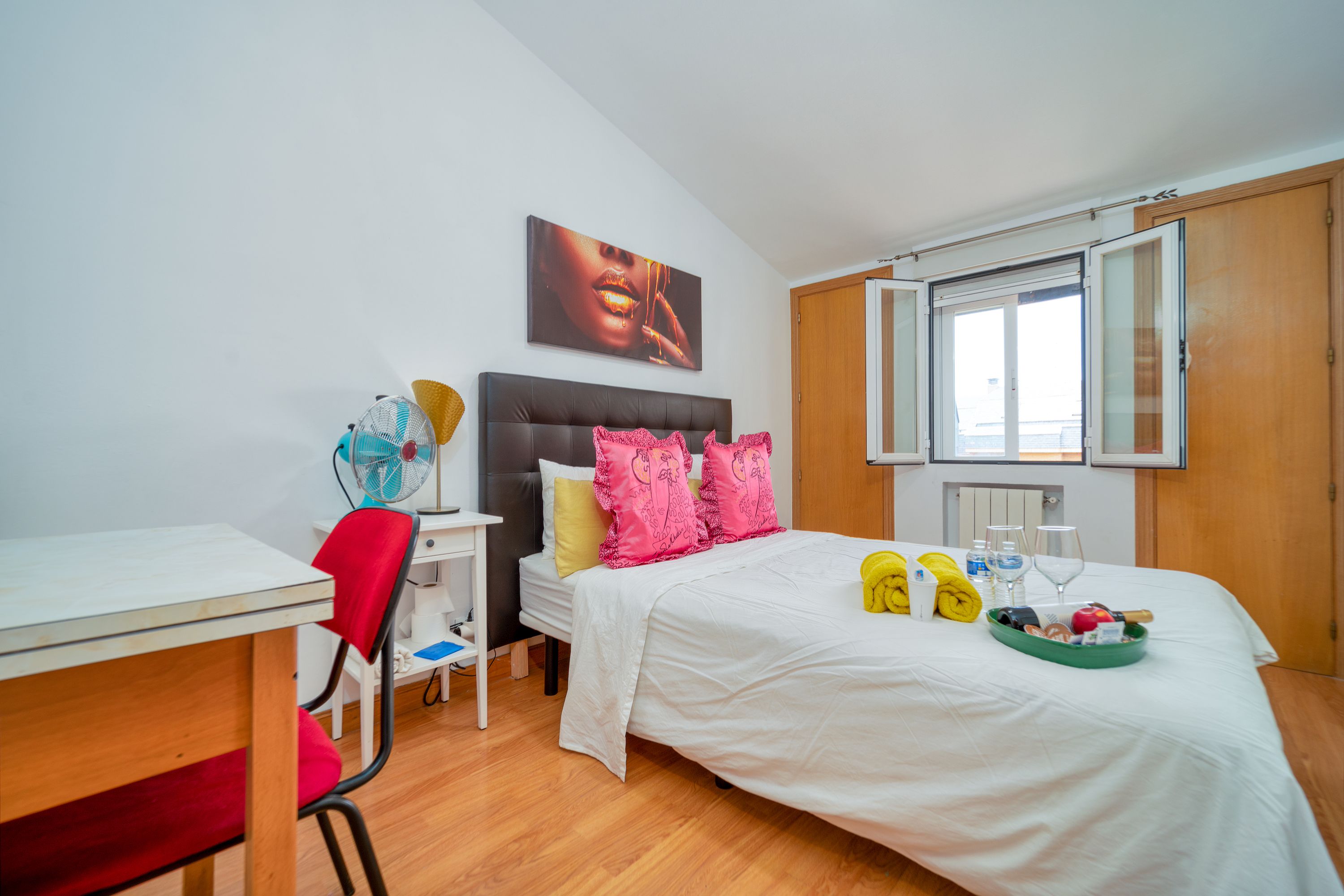 A contemporary bedroom featuring chic decor, an open window, and vibrant accents on the bed, creating a cozy and inviting atmosphere.