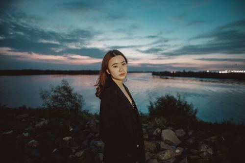 Free Portrait of a woman in a black blazer near a river at sunset with a scenic landscape view. Stock Photo