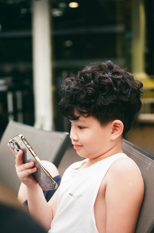 Free A Boy in White Tank Top Holding His Mobile Phone Stock Photo