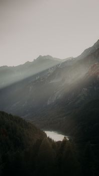 Majestic mountain valley with sun rays piercing through at dawn, creating a tranquil natural scene.