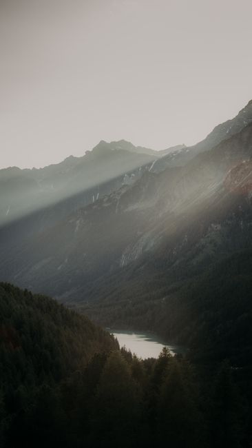 Majestic mountain valley with sun rays piercing through at dawn, creating a tranquil natural scene.