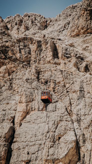 A lone cable car traversing a steep, rugged rock formation under a clear sky.