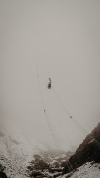 A solitary cable car traveling through a foggy mountain with snowy peaks.