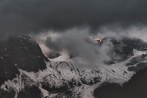Free A dramatic landscape of snowy mountain peaks partially covered by dense fog and dark clouds. Stock Photo