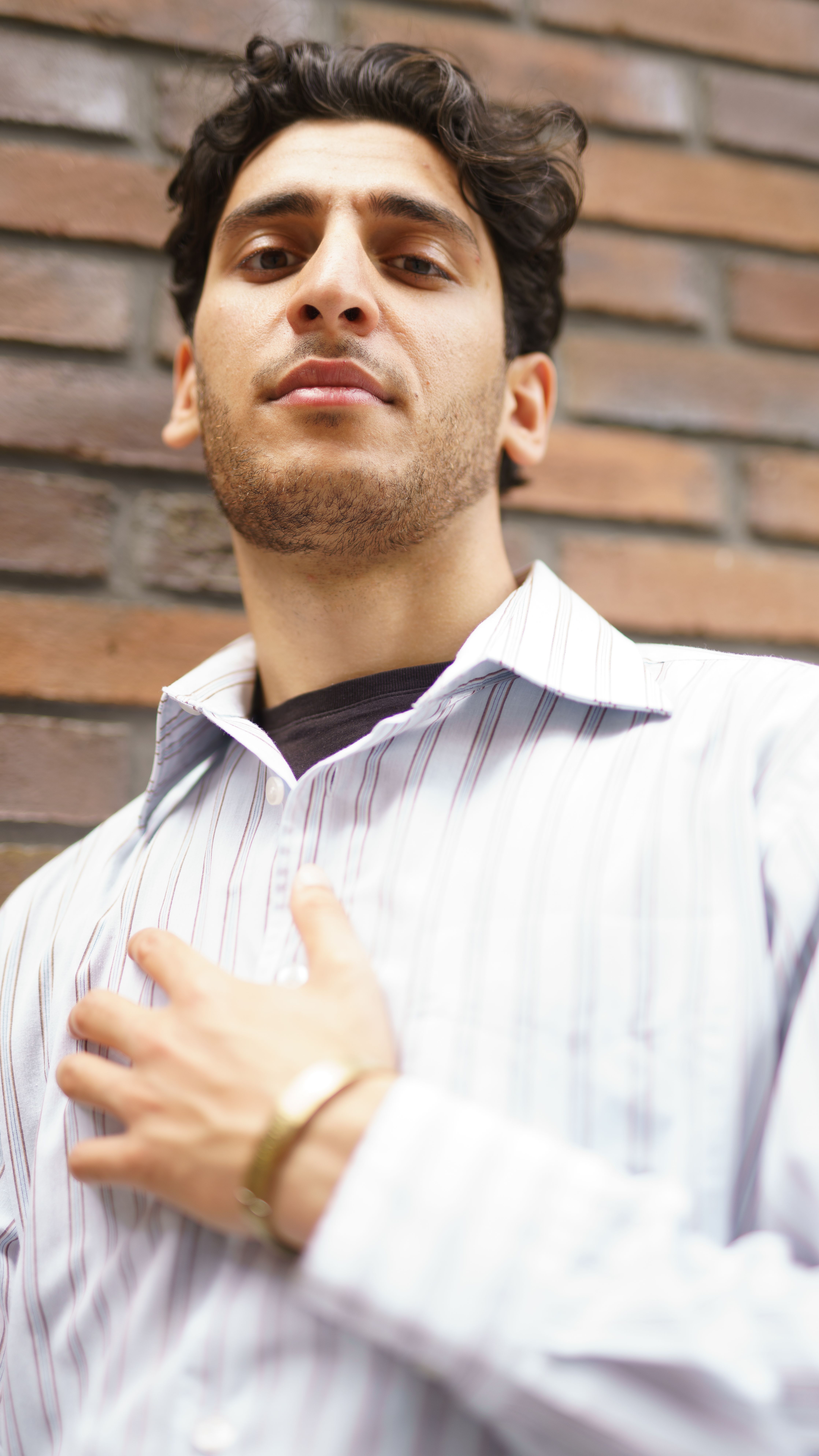 Young man in a stylish shirt poses confidently against a brick wall outdoors.