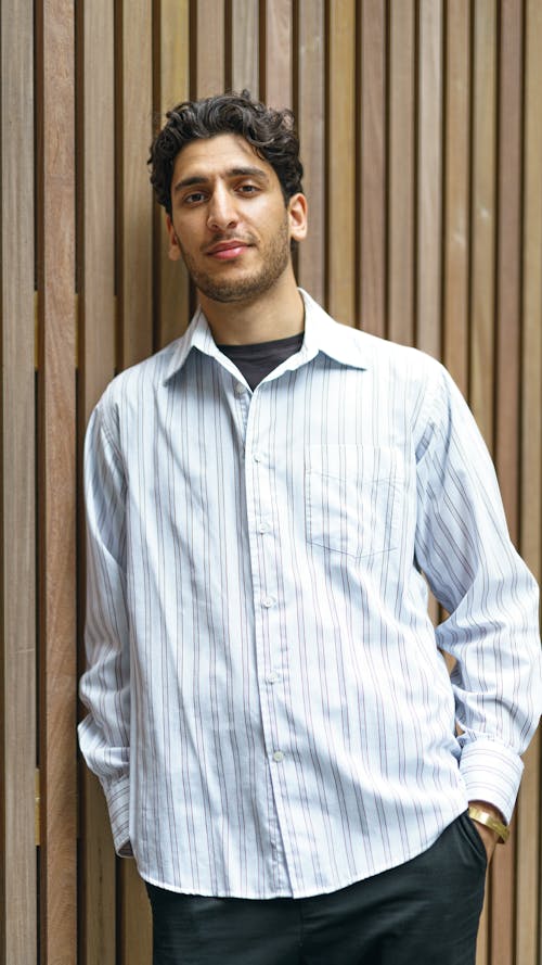 A Man in Striped Long Sleeves Leaning on a Wooden Wall