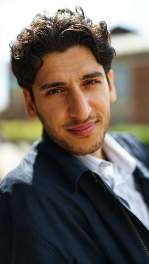 Free Portrait of a smiling young man with curly hair outdoors, wearing a black jacket. Stock Photo