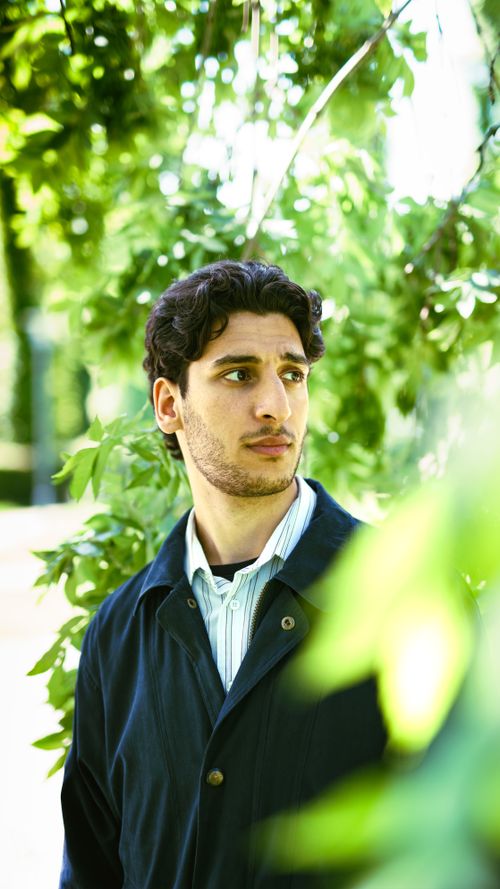 Free A young man stands thoughtfully in a lush green park, surrounded by foliage. Stock Photo
