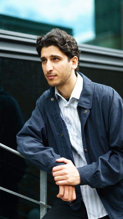 Free Portrait of a young man in blue jacket leaning on railing in an urban environment. Stock Photo