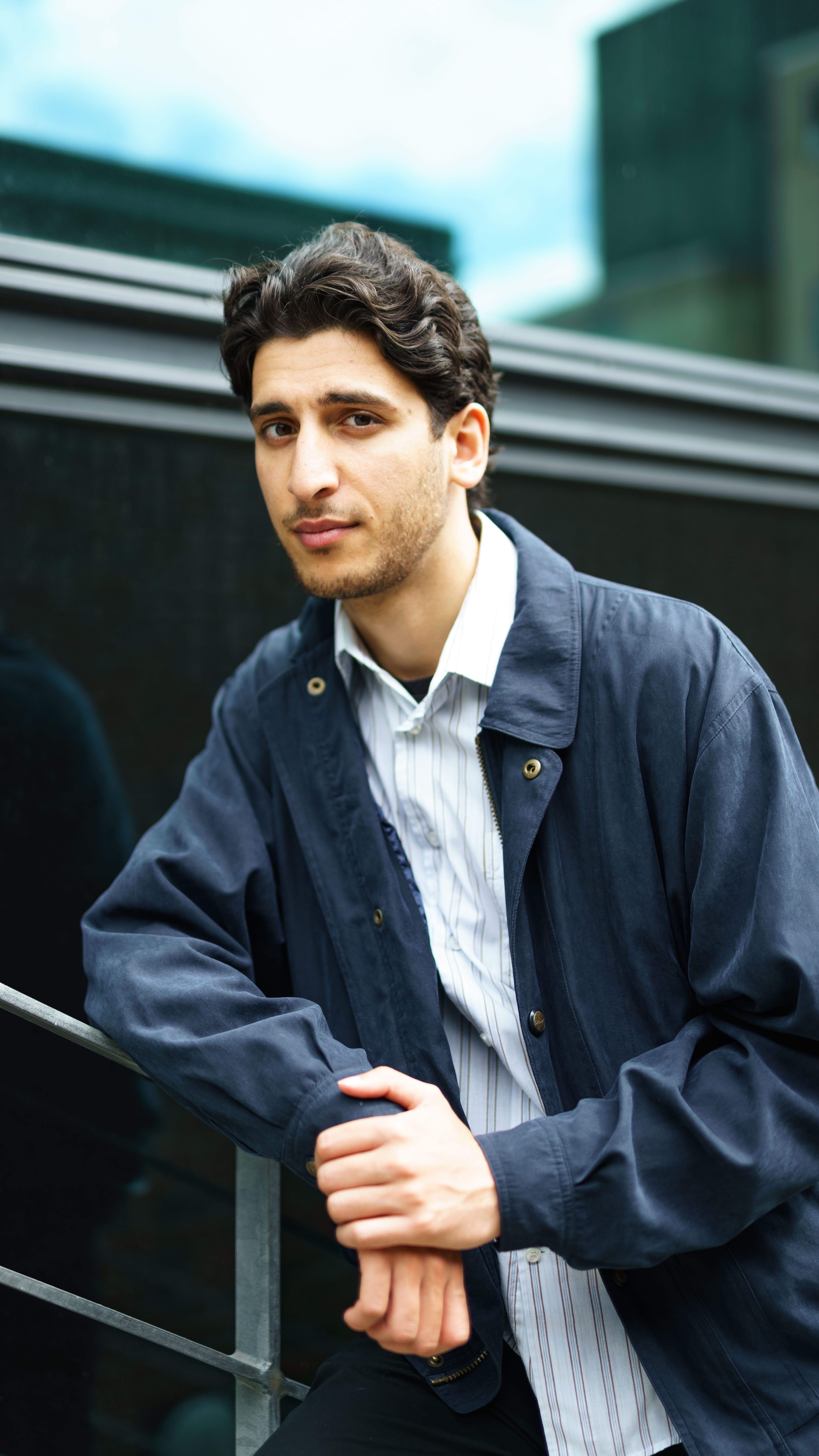 Man leaning casually against railing in outdoor urban environment, showcasing confidence.