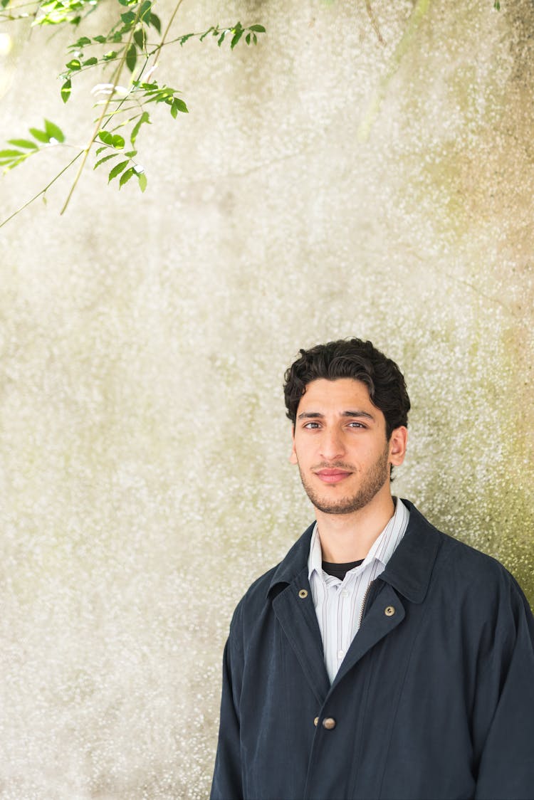 Man In Black Button Up Jacket Standing On Plain Wall