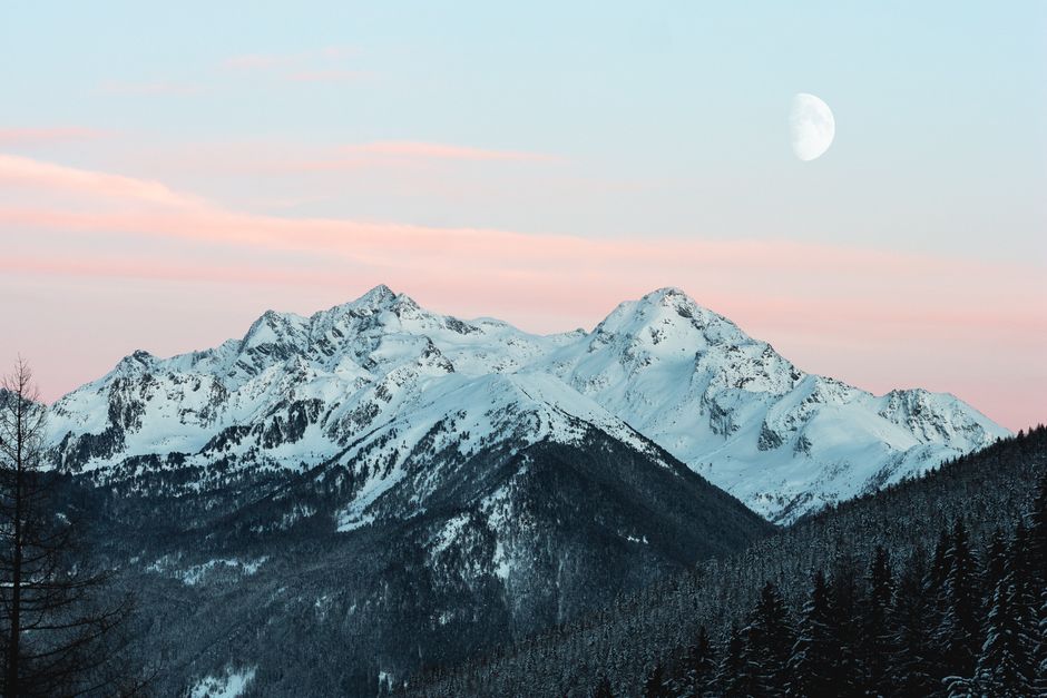 Majestic snow-covered mountain range with a rising moon and pink sunset sky.