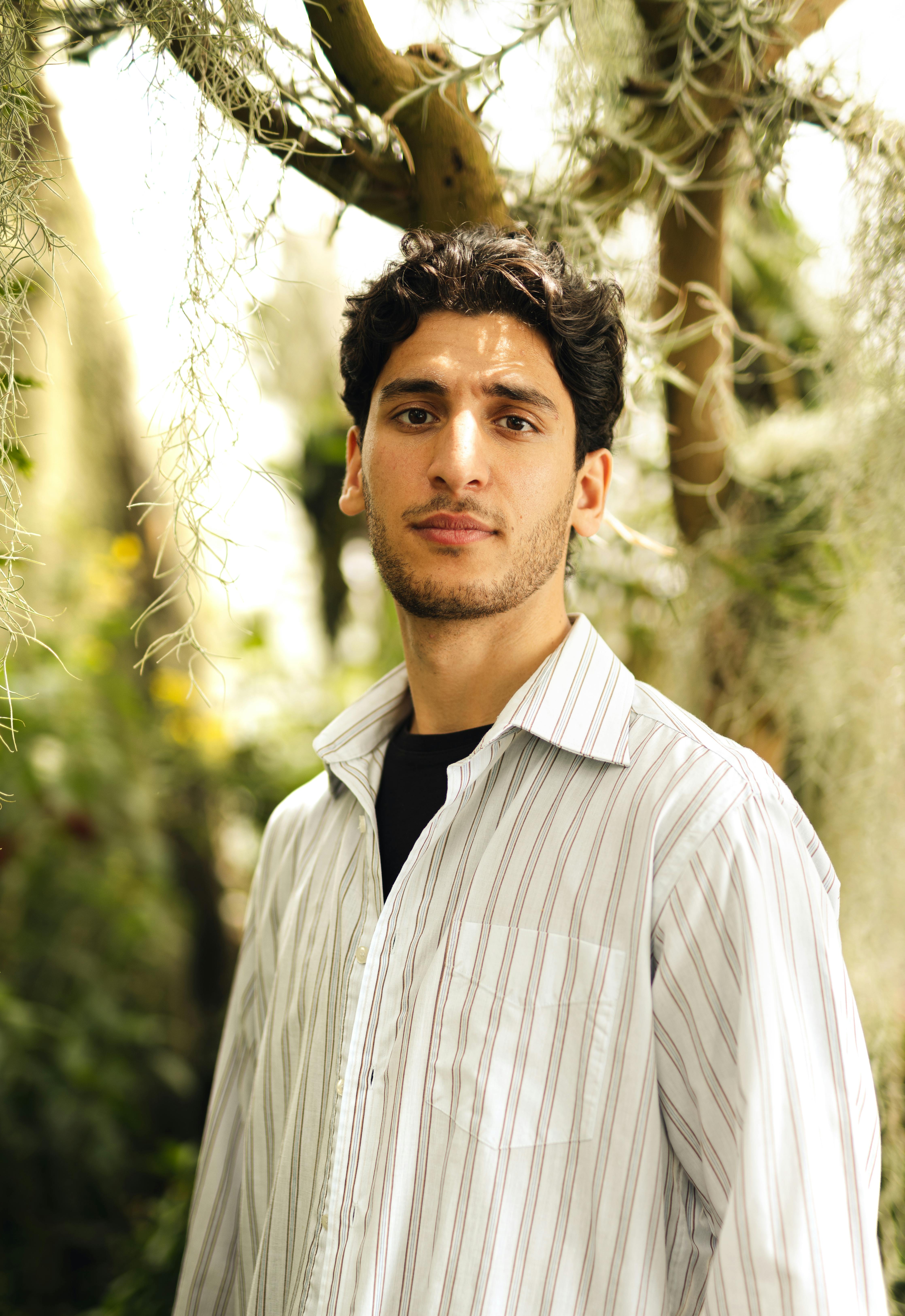 A portrait of a man with a serene expression, outdoors with lush greenery.