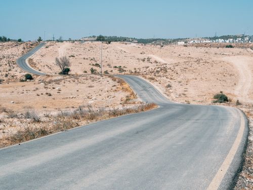 Free Lonely asphalt road winding through a vast desert landscape under a clear blue sky. Stock Photo