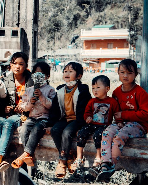Free Children sit together on a bench outdoors, showcasing a village atmosphere. Stock Photo