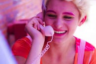 一位妆容鲜艳、面带微笑的女子在户外拿着一部复古粉色手机，散发着欢乐的气息