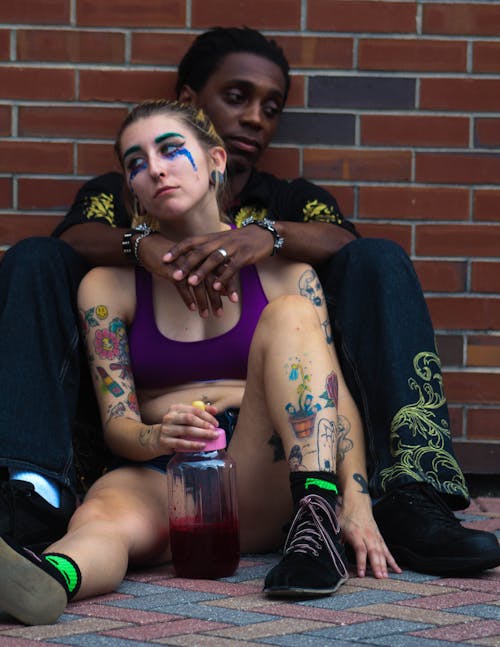 Woman And Man Sitting On Ground While Leaning On Wall