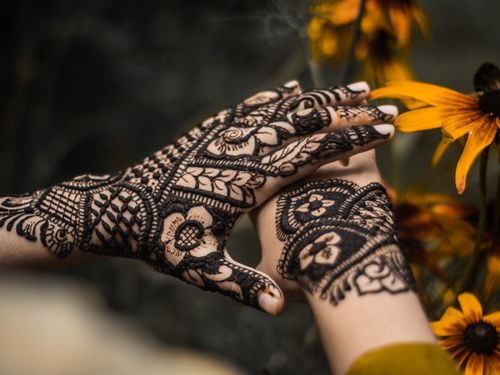 Free Close-up of beautifully decorated hands with henna designs surrounded by vibrant yellow flowers. Stock Photo