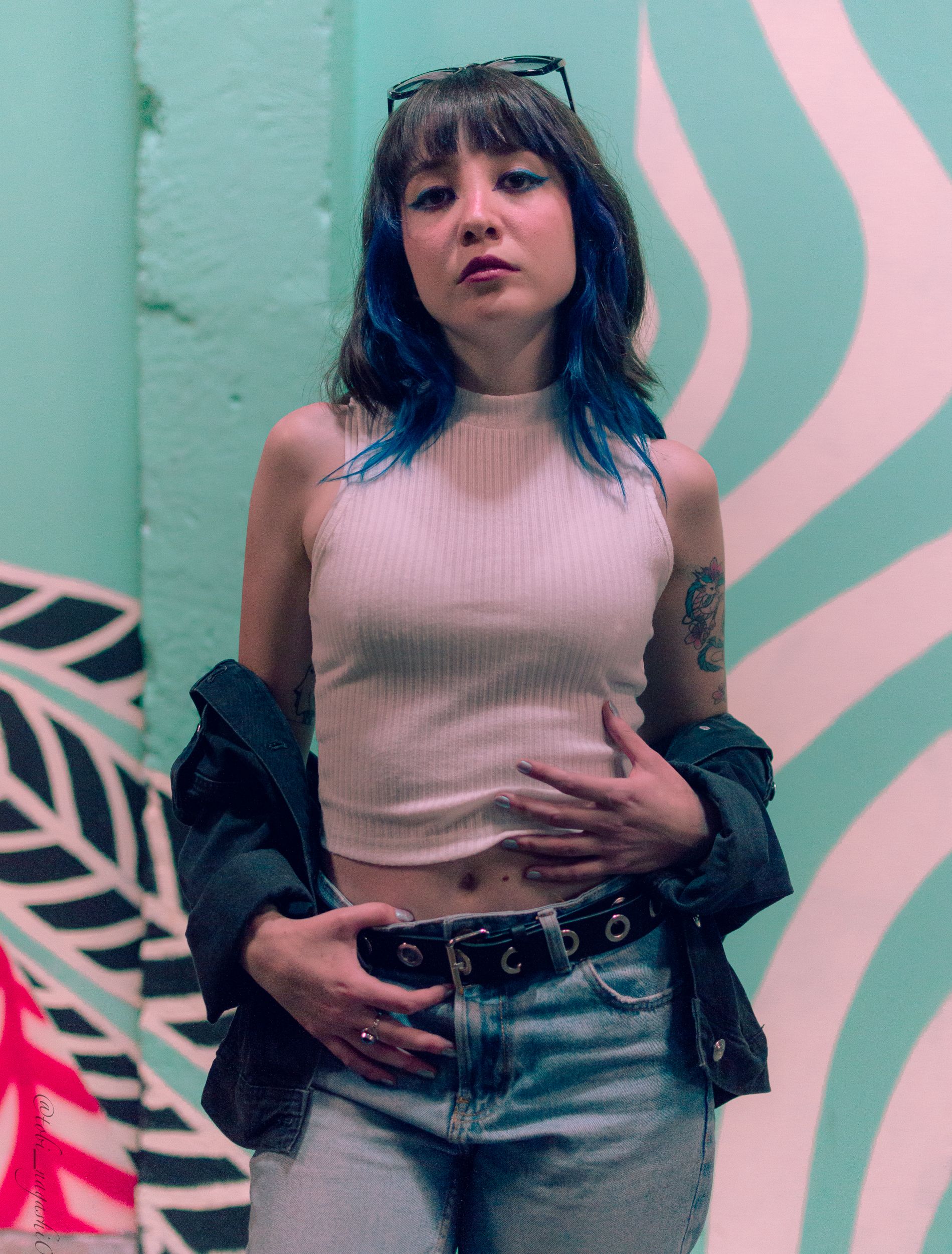 Stylish woman with blue highlights and tattoos poses confidently in urban setting.