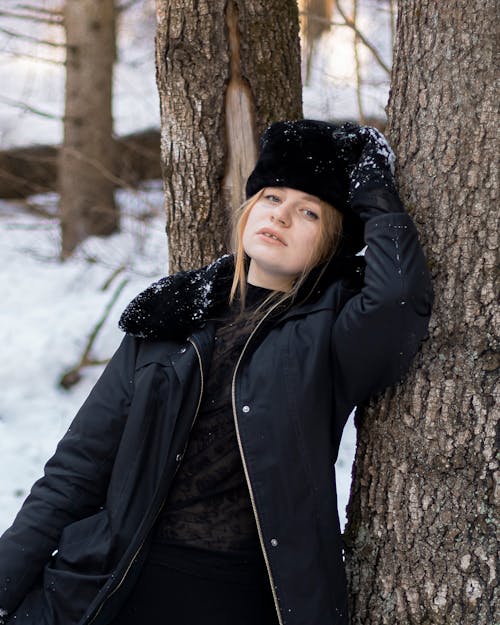 A Woman in Black Jacket Leaning on a Tree Trunk