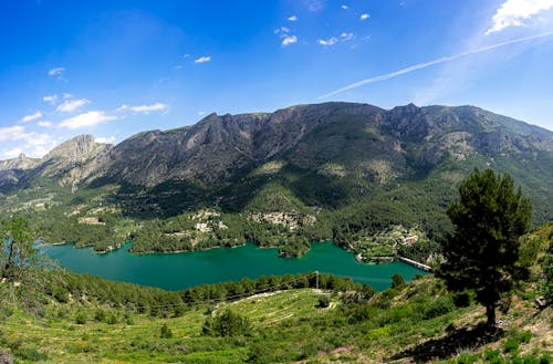 An Aerial Photography of a Lake Between Green Trees on Mountain Under the Blue Sky and White Clouds
