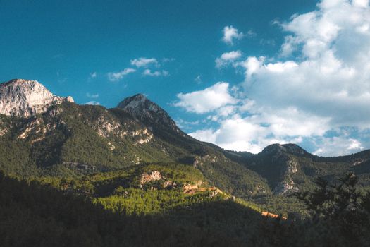 Breathtaking view of mountains and forest under a blue sky with clouds.