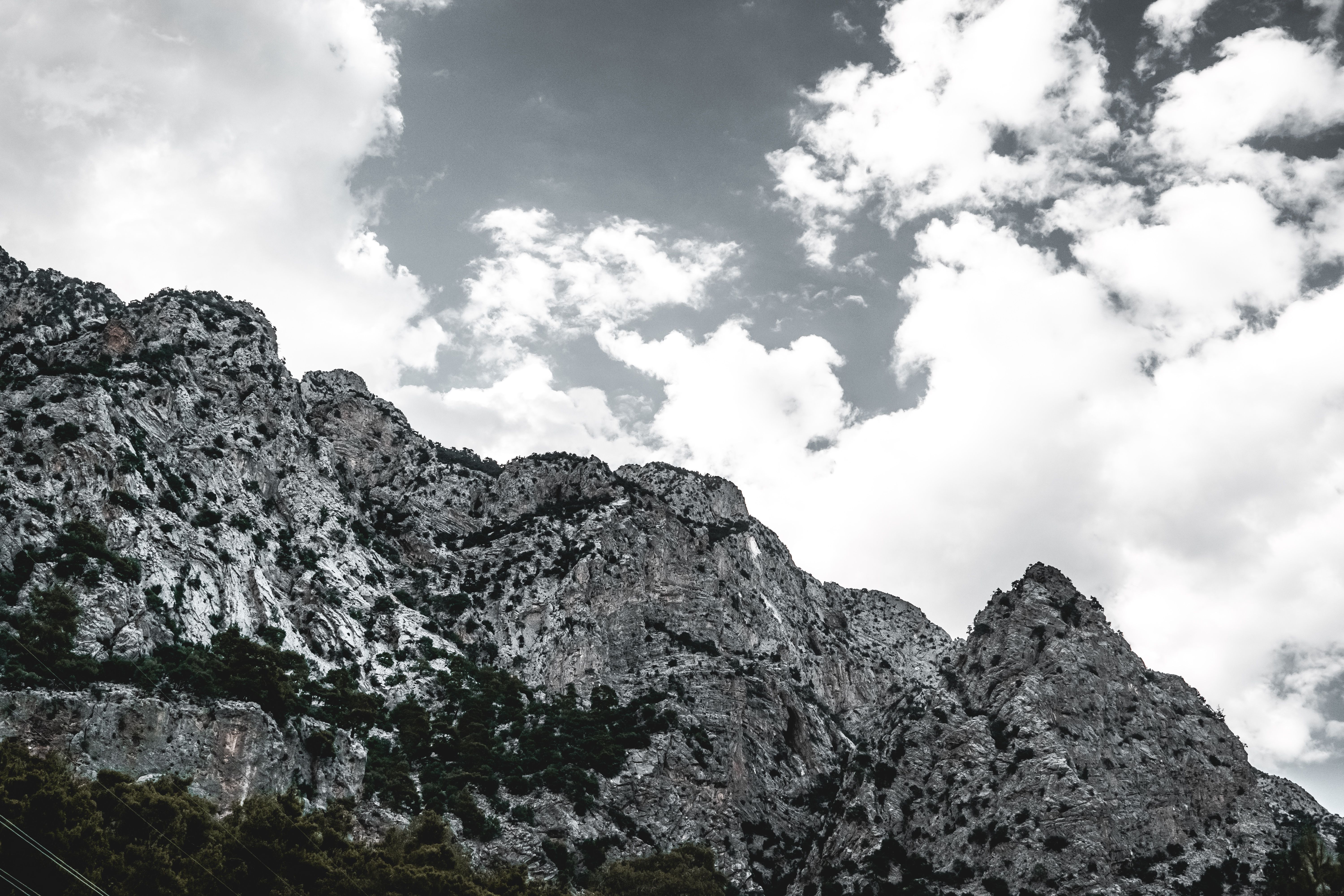 Grayscale Photo of Cloudy Sky above a Rocky Mountain · Free Stock Photo