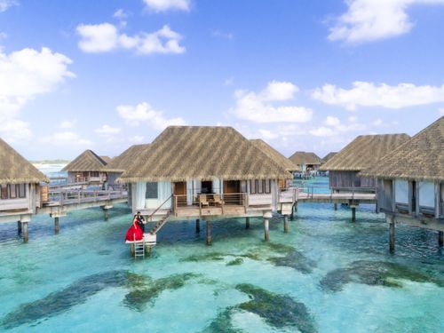 Free Overwater villa with couple in red dress in a tropical paradise setting. Stock Photo