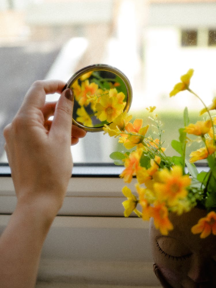 Hand Holding A Mirror With A Reflection Of Yellow Flowers