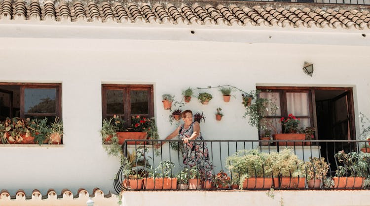 Woman Standing On Balcony With Potted Plants