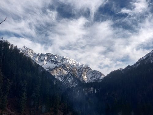 Free Majestic snow-covered mountains under a cloudy sky with lush forest at the base. Stock Photo