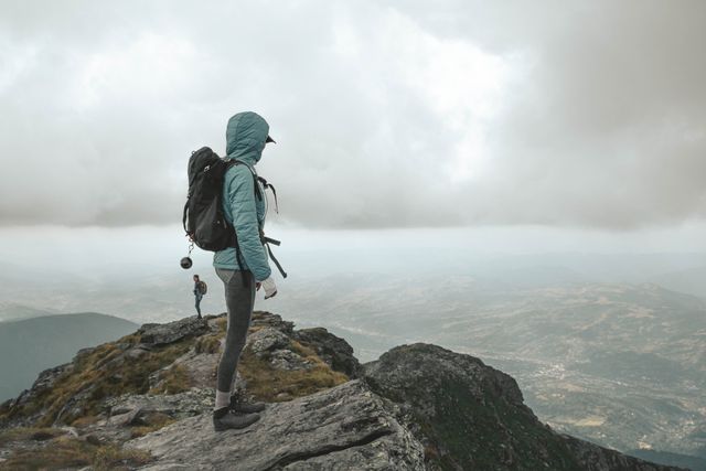 A lone hiker stands on a rocky mountain peak under a cloudy sky in Romania, embracing nature's beauty.