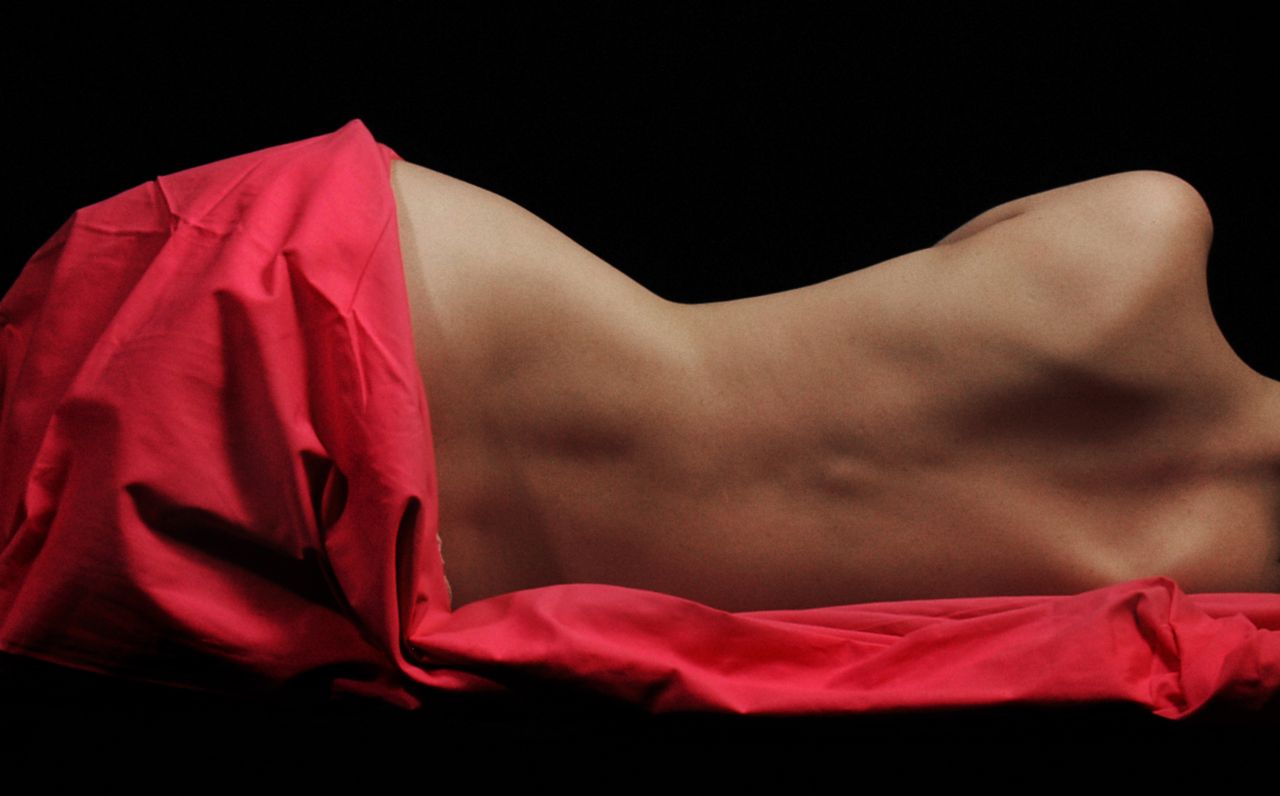 elegant nude art photo of a woman draped in red fabric on a black back